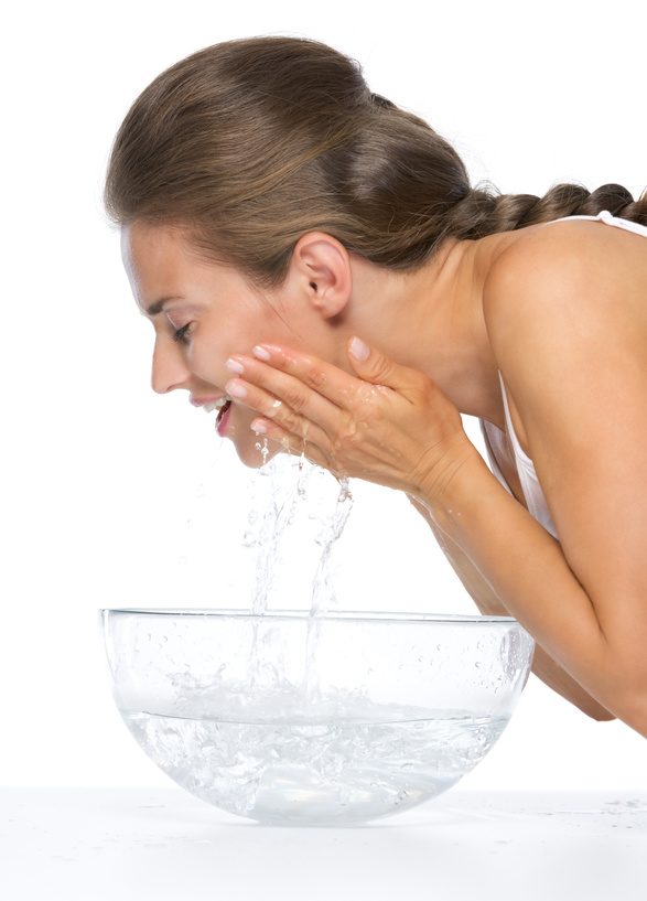 Profile portrait of happy young woman washing face in glass bowl with water